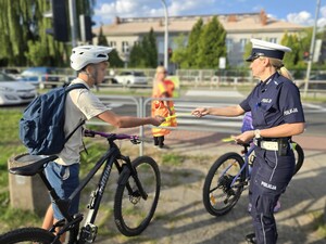 Policjantka wręcza odblask rowerzyście, który znajduje się przy przejściu dla pieszych
